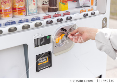 一名女子的手將硬幣放入自動販賣機 一名女子的手將硬幣放入自動販賣機 124869130