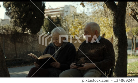 Elderly couple reading book and using phone in park. 124869244
