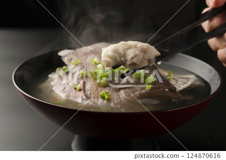 他用筷子從熱氣騰騰的魚湯裡夾起一條紅鯛魚。 他用筷子從熱氣騰騰的魚湯裡夾起一條紅鯛魚。 124870616