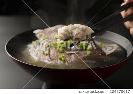他用筷子從熱氣騰騰的魚湯裡夾起一條紅鯛魚。 124870617