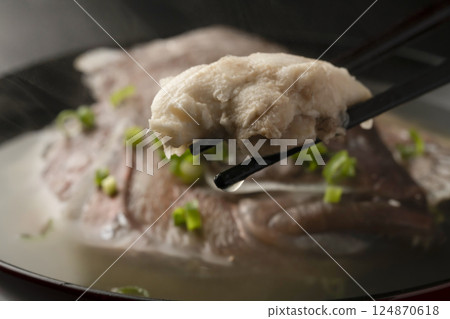 他用筷子從熱氣騰騰的魚湯裡夾起一條紅鯛魚。 124870618