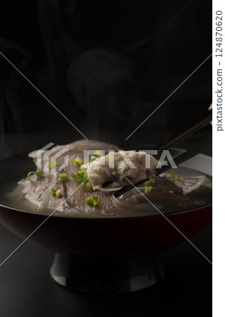 Using chopsticks, he lifts up a red sea bream from steaming fish soup. 124870620