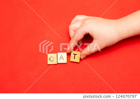 Child hand hands collecting word cat from wooden cubes on red background. Child hand hands collecting word cat from wooden cubes on red background. 124870797
