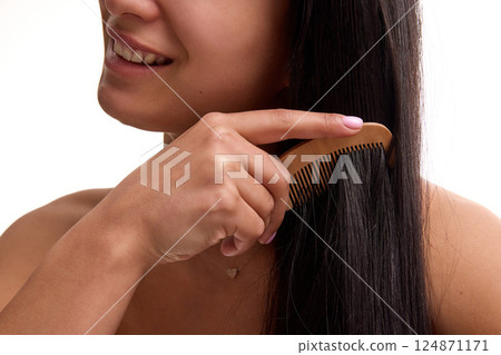 Cropped image of smiling woman taking care after her long black hair, combing with wooden comb against white background. 124871171