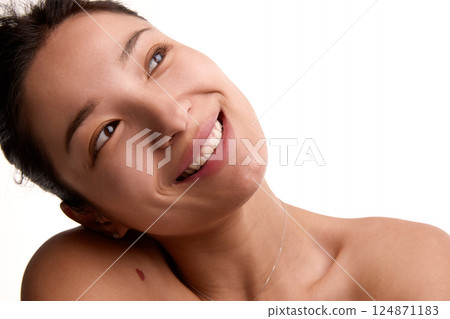 Portrait of smiling young Korean woman with glowing smile and perfect skin looks up in soft light against white background. 124871183