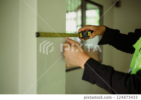 Close up of worker using measuring tape to check wall dimensions at a construction site Close up of worker using measuring tape to check wall dimensions at a construction site 124873433