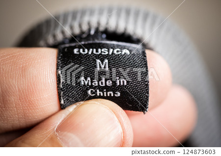 Extreme close-up of a black clothing tag labeled Made in China held between fingers Extreme close-up of a black clothing tag labeled Made in China held between fingers 124873603
