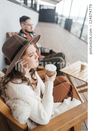 A young couple is arguing on a date. They are sitting at a table in a cafe on the veranda. The woman in the hat is upset and looks away anxiously. 124874779