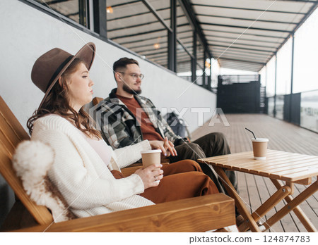 A young couple is arguing on a date. They are sitting at a table in a cafe on the veranda. The woman in the hat is upset and looks away anxiously. A young couple is arguing on a date. They are sitting at a table in a cafe on the veranda. The woman in the hat is upset and looks away anxiously. 124874783