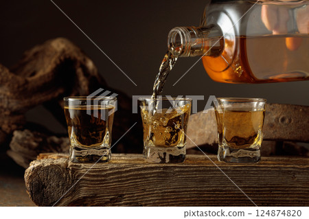 Whiskey is poured from a bottle into a shots. Whiskey is poured from a bottle into a shots. 124874820