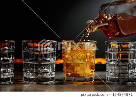 Whiskey is poured into a glass with ice. 124874871