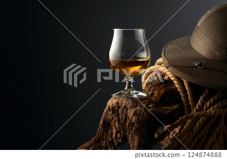 Snifter of brandy, cork tropical colonial helmet and rope on a old wooden snag. 124874888