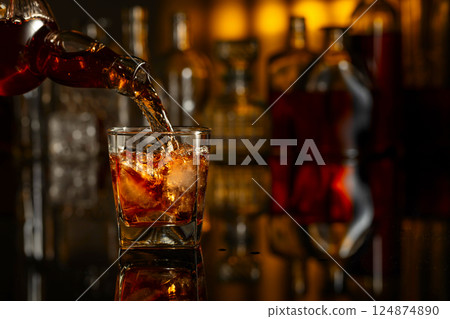 Whiskey is poured from a bottle into a glass with ice. 124874890