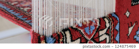 Manufacturing process, weaving of a traditional wool oriental red carpet with an intricate floral pattern, decorative elements. banner Manufacturing process, weaving of a traditional wool oriental red carpet with an intricate floral pattern, decorative elements. banner 124875469