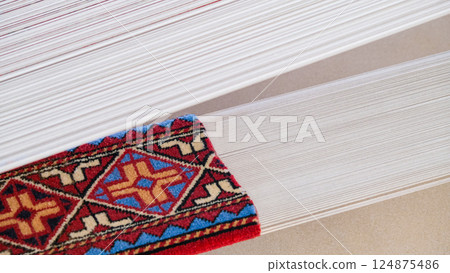Manufacturing process, weaving of a traditional wool oriental red carpet with an intricate floral pattern, decorative elements Manufacturing process, weaving of a traditional wool oriental red carpet with an intricate floral pattern, decorative elements 124875486