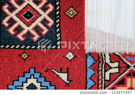 Manufacturing process, weaving of a traditional wool oriental red carpet with an intricate floral pattern, decorative elements Manufacturing process, weaving of a traditional wool oriental red carpet with an intricate floral pattern, decorative elements 124875487