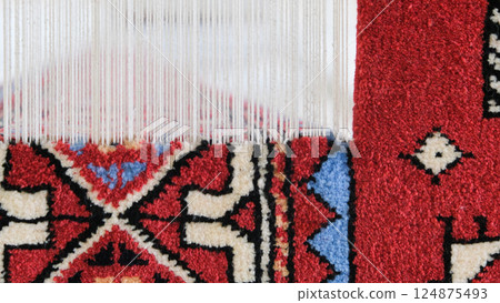 Manufacturing process, weaving of a traditional wool oriental red carpet with an intricate floral pattern, decorative elements Manufacturing process, weaving of a traditional wool oriental red carpet with an intricate floral pattern, decorative elements 124875493