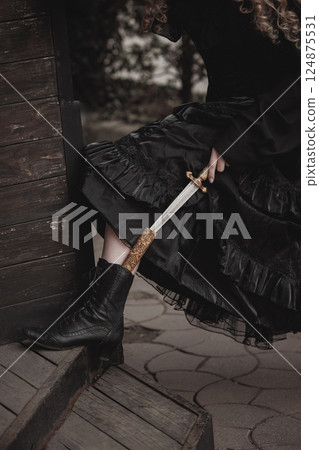 Close-up of woman's boot with gold-detailed dagger strapped beneath dark skirt. Female warrior. Suitable for noir story or mystery. Close-up of woman's boot with gold-detailed dagger strapped beneath dark skirt. Female warrior. Suitable for noir story or mystery. 124875531