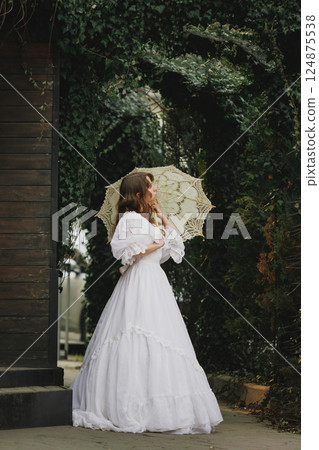Side view of elegant woman with delicate umbrella under ivy arch, soft glance over shoulder. Suitable for poetic novel or mystery. Side view of elegant woman with delicate umbrella under ivy arch, soft glance over shoulder. Suitable for poetic novel or mystery. 124875538