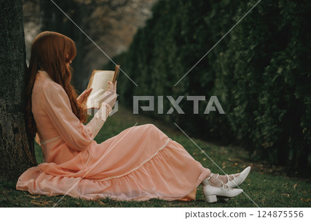She leans by tree trunk, long dress pooling on grass, pages open in lap, immersed in tales older than time. She leans by tree trunk, long dress pooling on grass, pages open in lap, immersed in tales older than time. 124875556