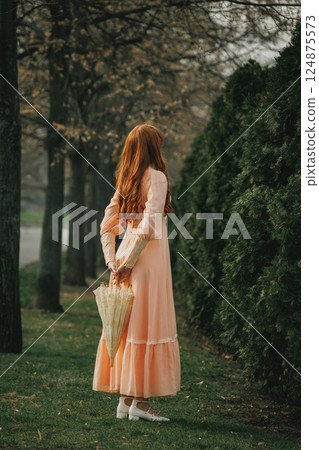 She turns from the world, face unseen, guarding secrets behind cascading curls, with umbrella like relic of bygone time. 124875573