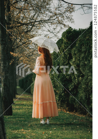 Side view of woman in vintage dress with parasol, caught in afternoon light, pausing in silence with unseen thoughts. Side view of woman in vintage dress with parasol, caught in afternoon light, pausing in silence with unseen thoughts. 124875582