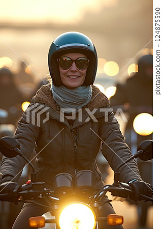 Vertical photo of a smiling middle aged female motorcyclist in sunglasses skillfully maneuvering through city streets on a powerful bike. 124875590