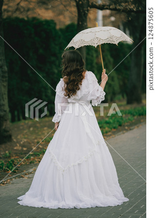 Mysterious figure in white with long curls walking among trees, with umbrella, autumn leaves glowing above. Concept of fantasy 124875605