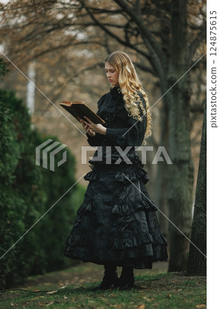 Victorian woman,wearing black lace dress, with golden hair reading ancient book in park alley under golden trees. Concept of vintage, fantasy Victorian woman,wearing black lace dress, with golden hair reading ancient book in park alley under golden trees. Concept of vintage, fantasy 124875615