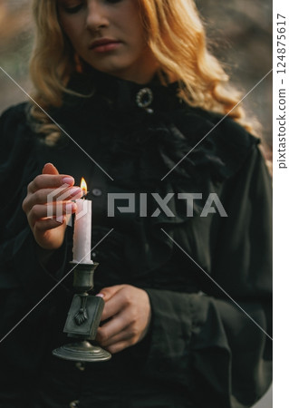 Close-up of woman's hand lighting candle, dressed in vintage black blouse, symbolic of ritual, remembrance or hidden secrets. Close-up of woman's hand lighting candle, dressed in vintage black blouse, symbolic of ritual, remembrance or hidden secrets. 124875617