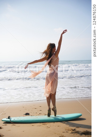 Calm ballerina in pink stands on pointe shoes on surfboard near calm sea  124876150