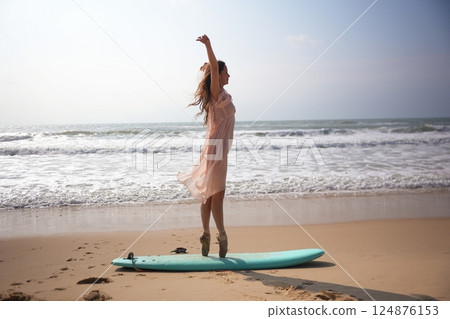Modern artistic concept of ballerina posing en pointe on surfboard at the beach 124876153