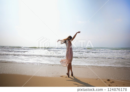 Light dress flows as ballerina stands en pointe on surfboard in ocean breeze Light dress flows as ballerina stands en pointe on surfboard in ocean breeze 124876178