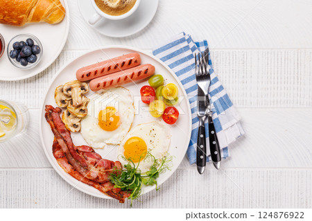 A classic breakfast plate featuring sunny-side-up eggs, crispy bacon, sausages, and fresh tomatoes 124876922