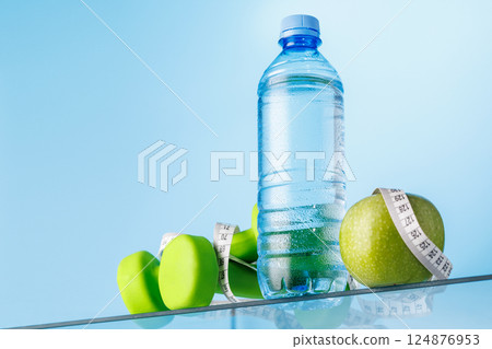 Bottle of water, green apple, and dumbbells on a glass table Bottle of water, green apple, and dumbbells on a glass table 124876953
