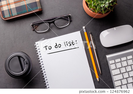 Organized work desk setup with PC, office supplies, coffee, and a notepad for writing a to-do list 124876962