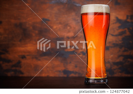 A tall glass of amber beer with frothy head 124877042