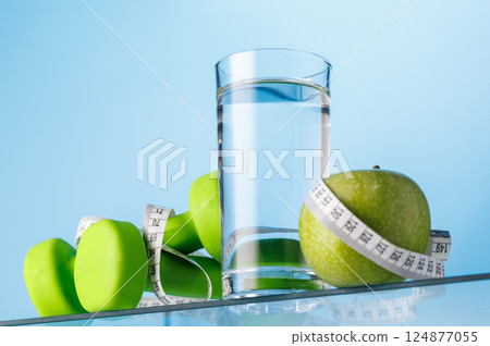 Glass of fresh water, green apple, and dumbbells on a glass table Glass of fresh water, green apple, and dumbbells on a glass table 124877055