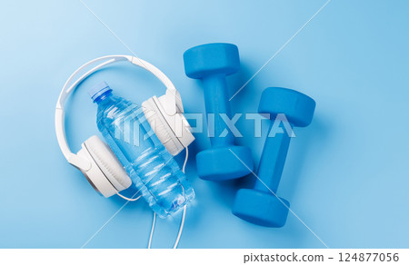 Flat lay of headphones and dumbbells over a bright blue background 124877056