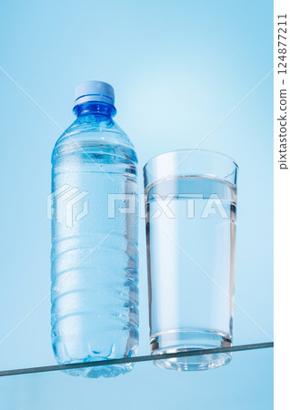 Glass of fresh water and bottle on a glass table against a vibrant blue background Glass of fresh water and bottle on a glass table against a vibrant blue background 124877211