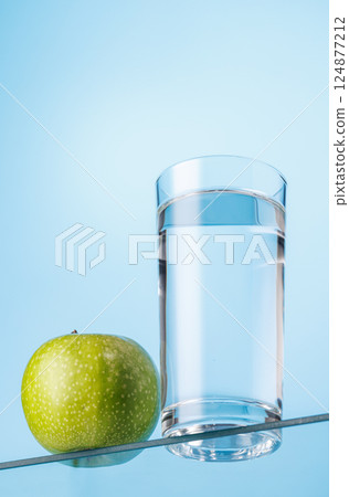 Glass of fresh water and a green apple on a glass table 124877212