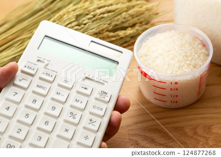 Hand holding a measuring cup of rice and a calculator 124877268