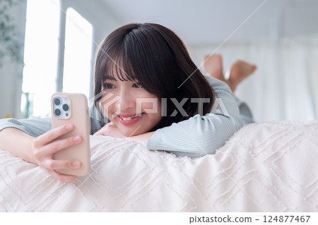A young woman lying down and operating a smartphone A young woman lying down and operating a smartphone 124877467