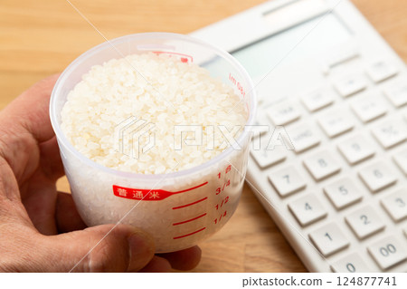 手拿著量杯的米和一個計算器 124877741