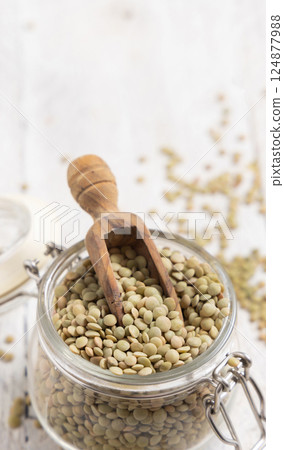 Glass jar full of raw green lentils with a wooden scoop on white table closeup. Dried legumes Glass jar full of raw green lentils with a wooden scoop on white table closeup. Dried legumes 124877988