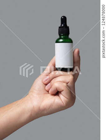 Hand holding dropper bottle with blank label against grey close up, cosmetic mockup 124878000
