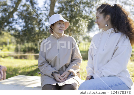 Senior woman and young caregiver talking on bench in park 124878378