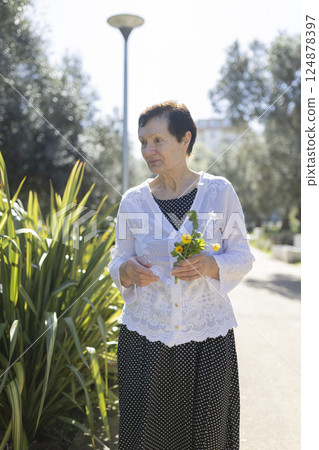 Elderly woman holding flowers enjoying walk in public park 124878397
