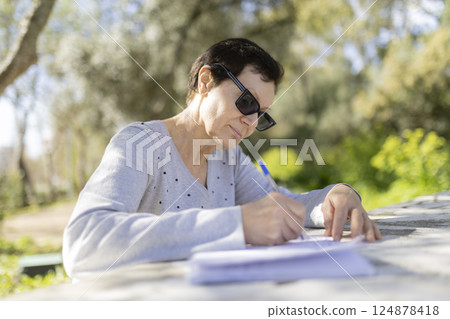 Senior woman writing outdoors on a sunny day 124878418