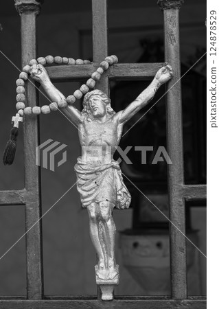 Statue of crucified figure adorned with rosary beads attached to iron bars in a somber setting 124878529